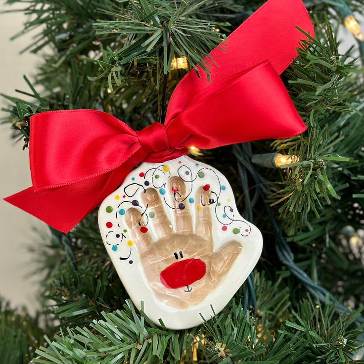 a christmas ornament hanging on a tree with a red ribbon and hand print