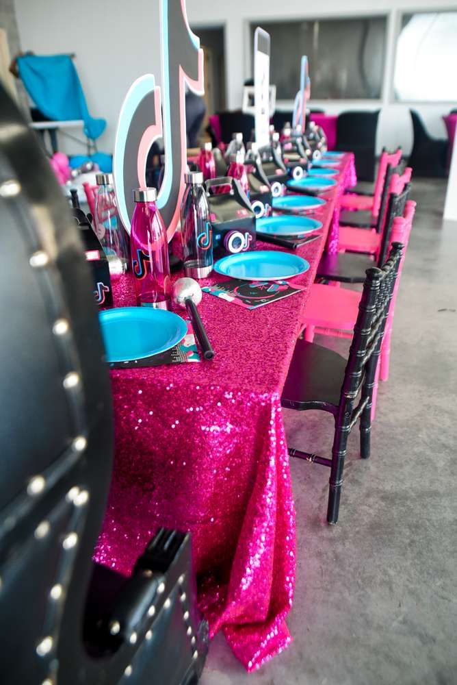 there is a long table set up with blue and pink plates, silverware, and black chairs