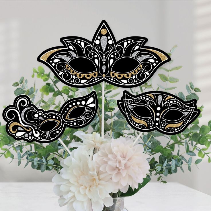 a vase filled with white flowers next to a black and gold mask cake topper