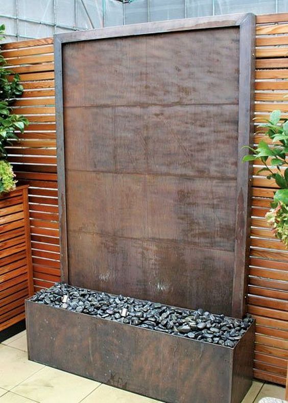 an outdoor water feature surrounded by wooden slats and plants on the side of a building