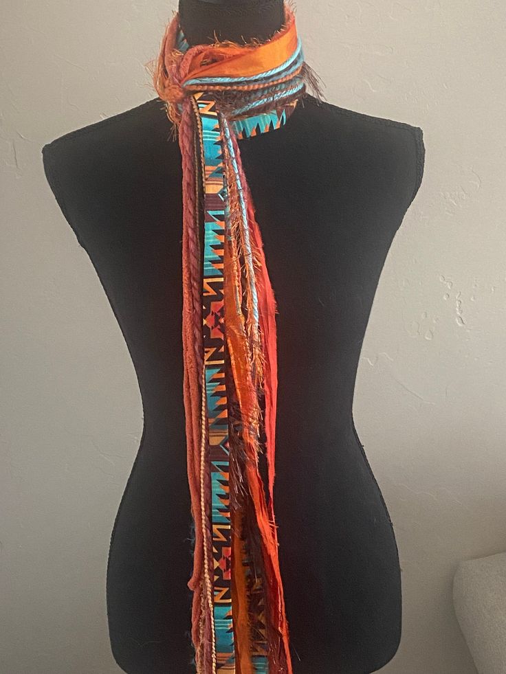 "This handmade scarf consists of a variety of yarn strands and hand sewn fabric ribbon in lovely southwest colors, orange rust yellow brown and turquoise.  I utilize a variety of yarns in each of my scarves and no two are ever the same.   Each scarf is made up of a selection of Sari Silk, Eyelash, Ribbon, Ladder, Fuzzy, Sparkly, Pouf Pom Pom, Boucle, Flag Ribbon, Nub, Pluscious, Hand Spun, and Brushbound. It is approximately 80\" long. This is an open fringe style, tied at center allowing for styling flexibility.  It is a medium weight scarf. Check out this YouTube link for a demonstration of the many ways that you can style this scarf: https://www.youtube.com/watch?v=5LYAEz777AU" Multicolor Bohemian Weaving Scarves, Bohemian Woven Scarves One Size, Bohemian Multicolor Woven Scarves, Bohemian Woven Scarf, Bohemian Weaving Scarf For Fall, Handmade Multicolor Scarves For The Beach, Handmade Multicolor Scarf For Beach, Handmade Multicolor Scarves For Beach, Multicolor Handwoven Bohemian Scarves