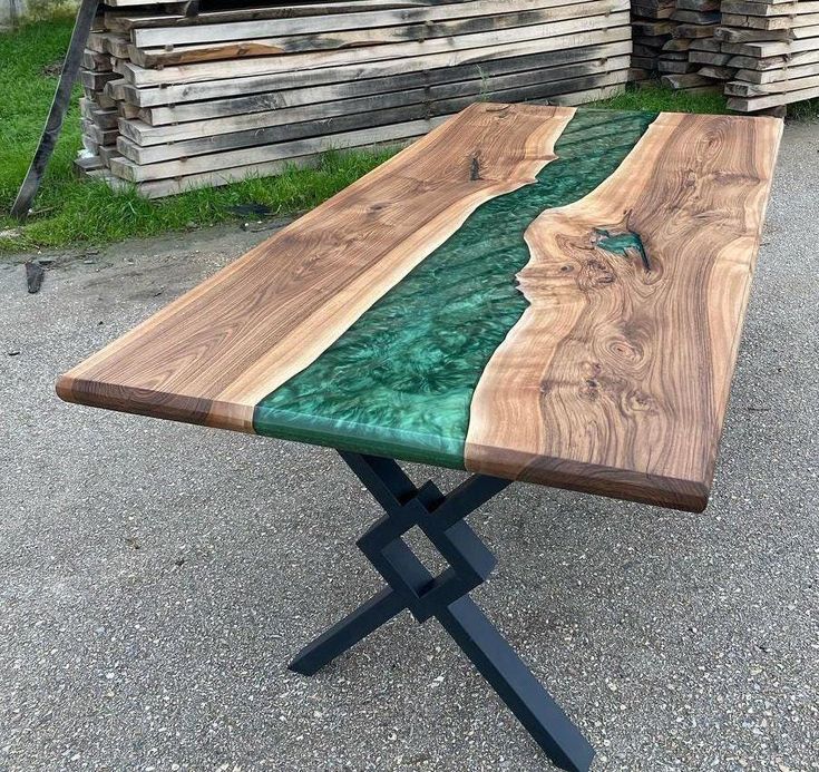 a table made out of wood with green glass on top and black metal legs, sitting in front of stacks of lumber