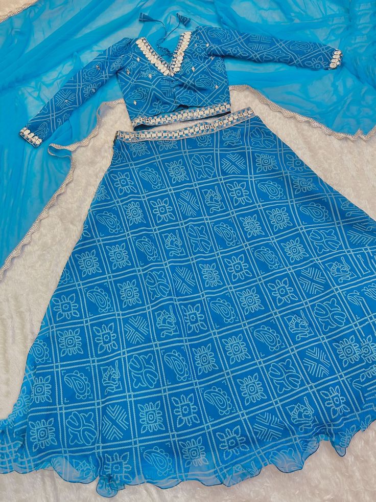 This beautiful sky-blue lehenga is perfect for festivals like Navaratri, special occasions, and weddings. The semi-stitched lehenga comes in a sky-blue color with bandhani print work, intricate thread, paper mirror, and sequin work on the waist.
The set includes a similar color georgette choli with bandhani print work, thread work, paper mirror, and sequins work, as well as a matching georgette dupatta with border work.
This lehenga choli set is its versatility. It can be dressed up for a festiv Blue Sharara For Navratri Festival, Blue Sharara For Navratri Festive Occasion, Blue Sharara For Navratri Festivities, Blue Dresses With Gota Work For Festive Season, Festive Blue Dresses With Gota Work, Festive Blue Dress With Gota Work, Blue Unstitched Cutdana Sets, Blue Gota Work Dresses For Diwali, Blue Floor-length Sets With Gota Work