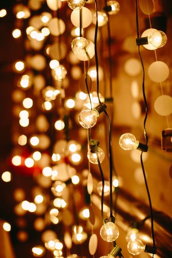 a bunch of lights that are hanging from the ceiling in front of a wall with candles on it