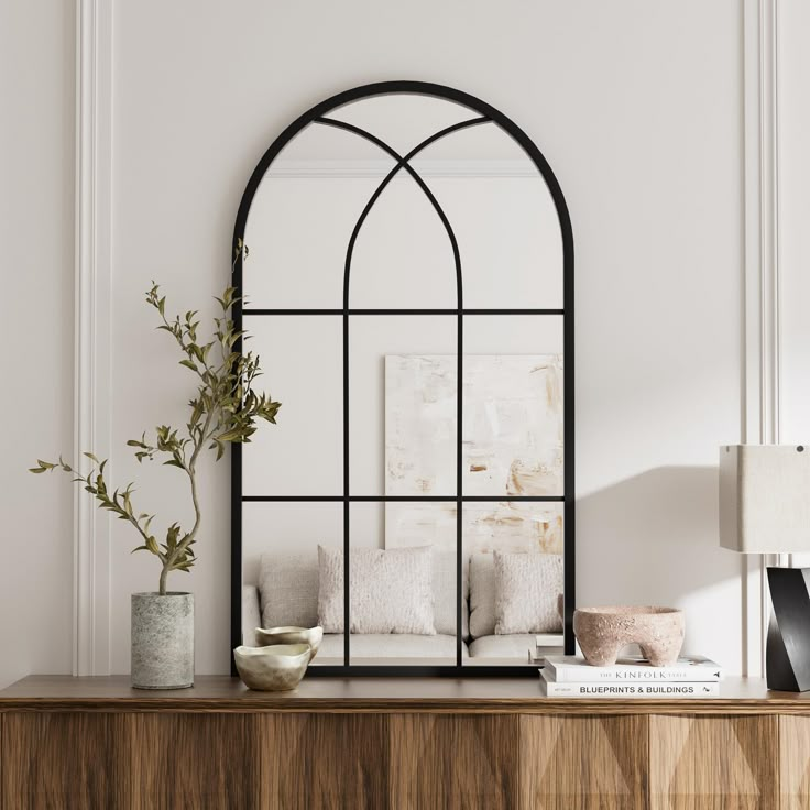 a living room with a large arched mirror on top of a wooden dresser next to a plant