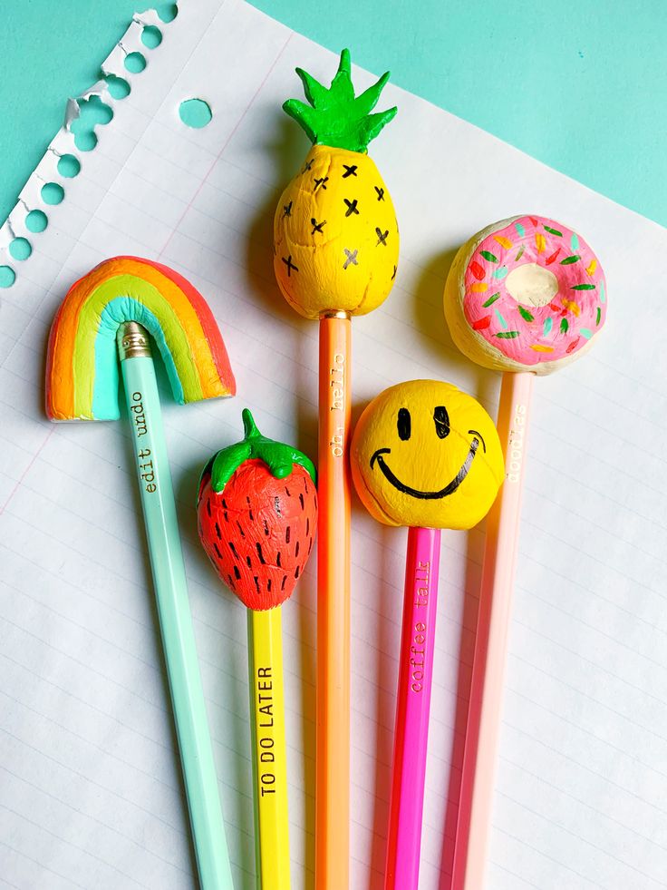 four pencils with smiley face, strawberry, donut and rainbow on them next to a notepad