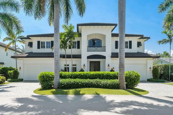 a large white house with palm trees in the front yard and landscaping on both sides