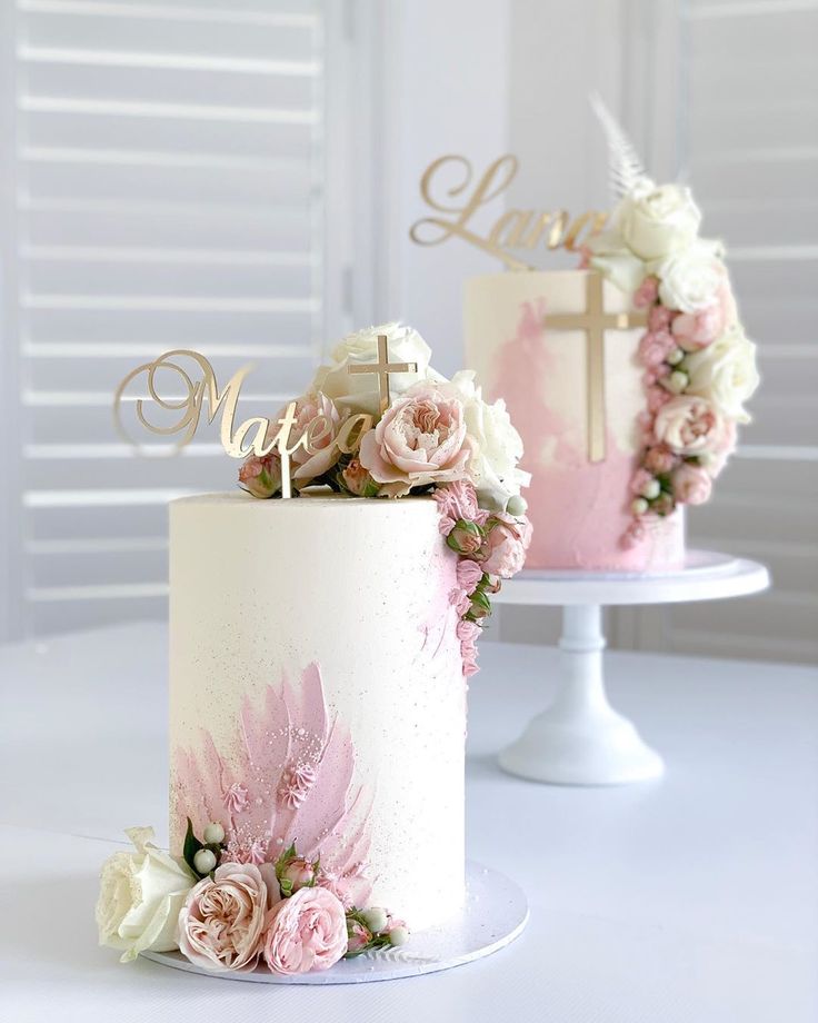 two wedding cakes decorated with pink and white flowers on top of each other, one has a cross