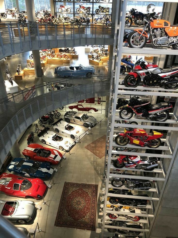 there are many cars and motorcycles on display in the building with people looking at them