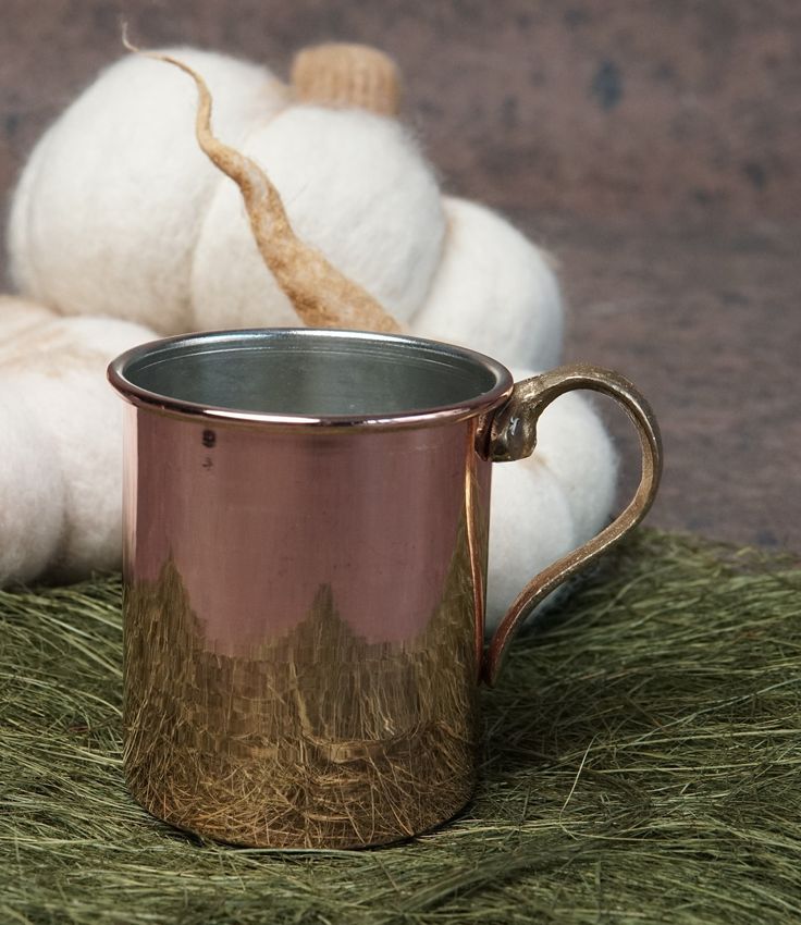 a copper mug sitting on top of green grass next to a white ball of yarn