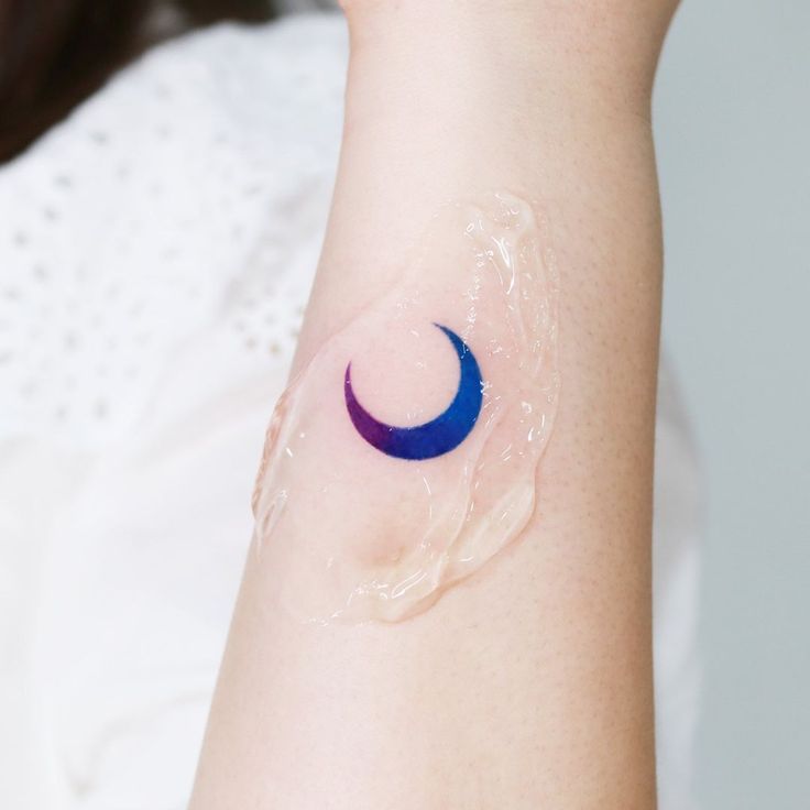 a woman's arm with a blue crescent tattoo on it