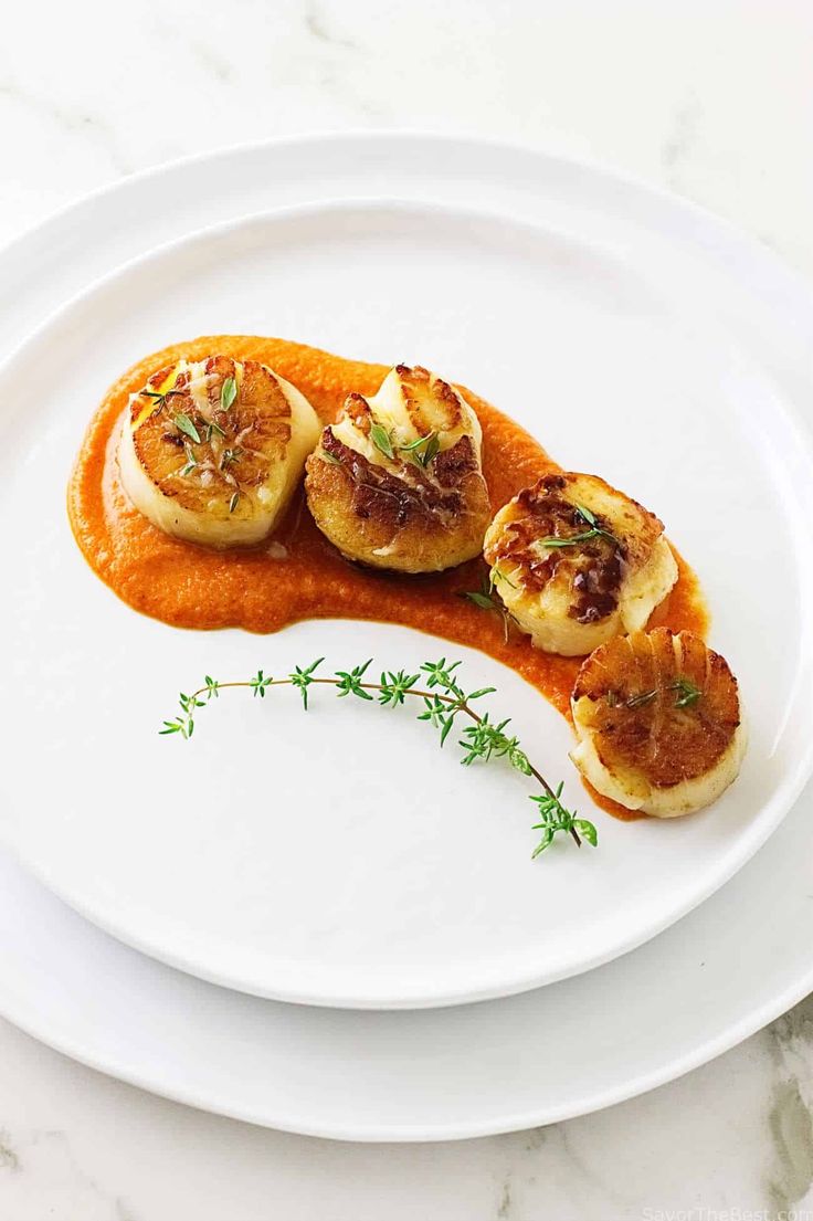 a white plate topped with scallops covered in sauce and garnished with herbs