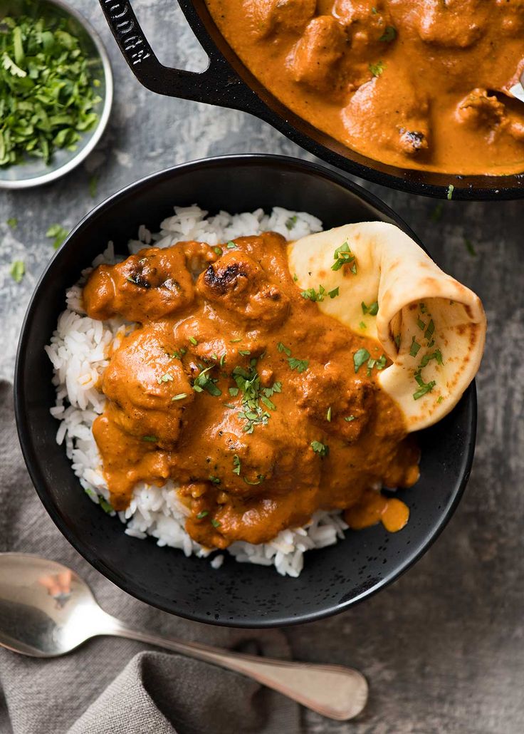 two black bowls filled with rice and meat covered in gravy next to silver spoons