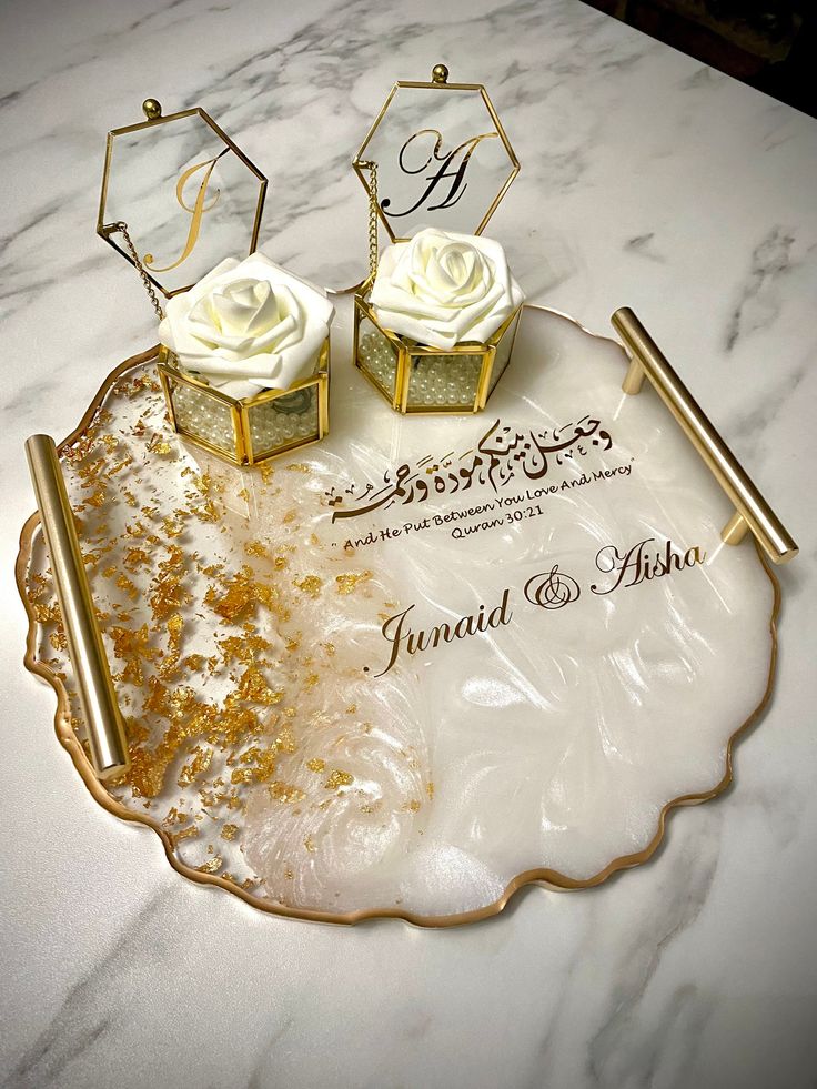 two white roses sitting on top of a marble tray with gold trim and matching napkins