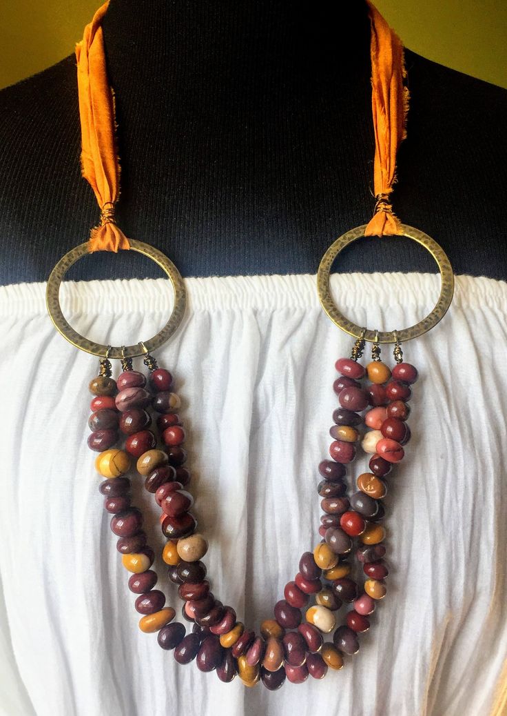 This handmade necklace earrings set features three strands of gorgeously shiny Mookaite gemstone beads in hues of mustard yellow to deep red and purple. I used a mustard yellow recycled sari silk ribbon to create a unique textural element to this necklace. The bronze rings add interest to it as well as add to the gold tones of the overall rich yellowness in this necklace.  The necklace has an overall length of 31 inches and cascades down on the chest in a beautiful curve.  Free shipping within US. Mookaite Rustic Gemstone Necklace, Boho Chic Long Necklace, Boho Necklace Beaded Necklace Mustard Yellow Sari Silk Jewelry Circle Necklace Adjustable Multi-strand Wooden Bead Jewelry, Multi-strand Gold Jewelry With Wooden Beads, Gold Multi-strand Jewelry With Wooden Beads, Bohemian Dangle Jewelry With Polished Beads, Handmade Bohemian Amber Beads, Bohemian Amber Beads With Natural Stones, Multi-strand Wooden Beads For Jewelry Making, Bohemian Polished Beads For Jewelry Making, Orange Wooden Beads For Jewelry Making