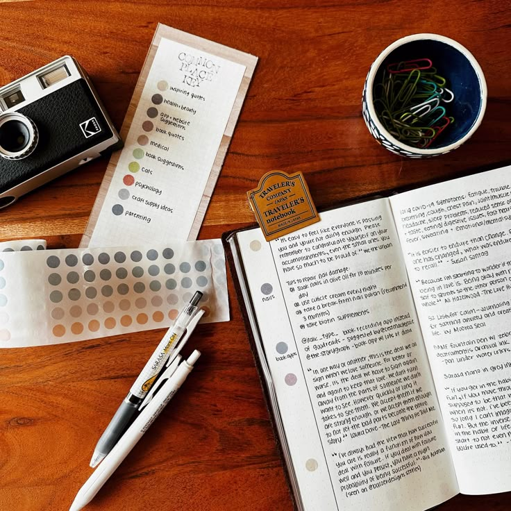 an open book sitting on top of a wooden table next to a pen and camera