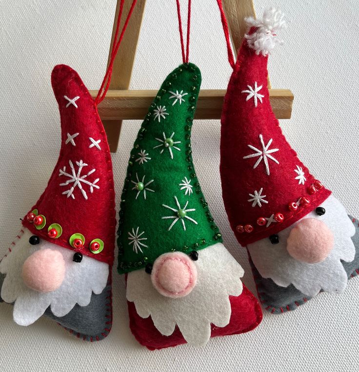 three christmas gnome ornaments hanging from a wooden rack