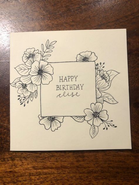 a happy birthday card with flowers on the front and bottom, sitting on a wooden table