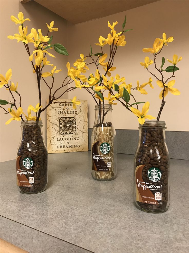 three jars with yellow flowers in them sitting on a counter top next to a sign