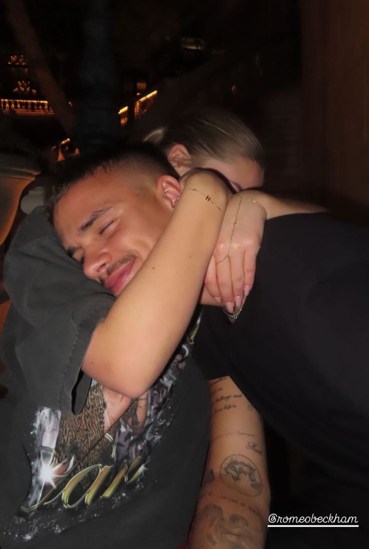 a man and woman hugging each other while they are sitting on a bench at night