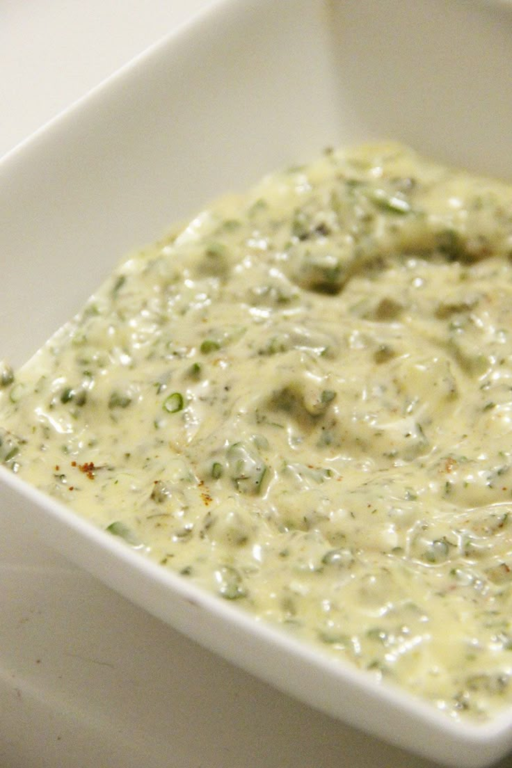 a square white bowl filled with cheese and broccoli sauce on top of a table