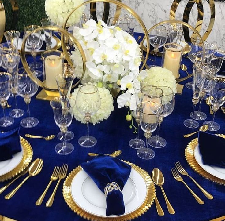 a blue table cloth with white flowers and gold trimmings is set for a formal dinner