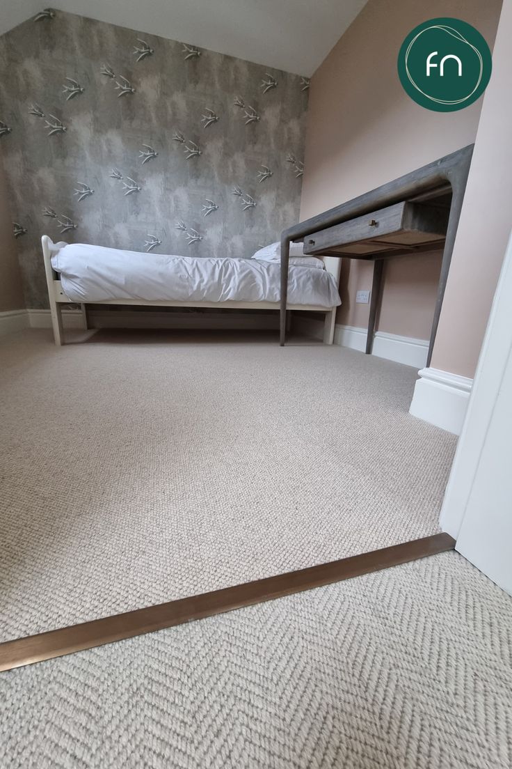 an empty room with a bed, desk and carpeted floor in front of a wallpapered wall