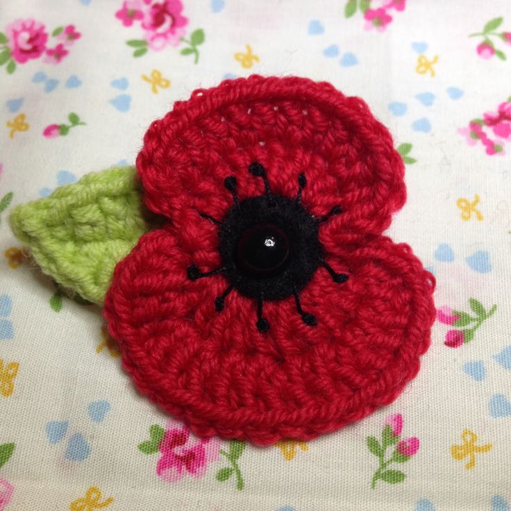 a crocheted red flower sitting on top of a white table covered in flowers