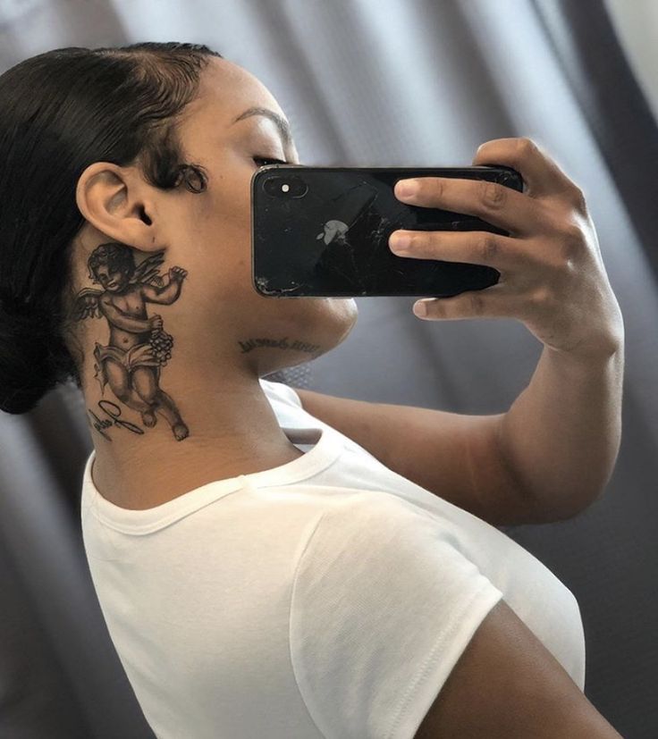 a woman taking a selfie with her cell phone in front of her neck tattoo