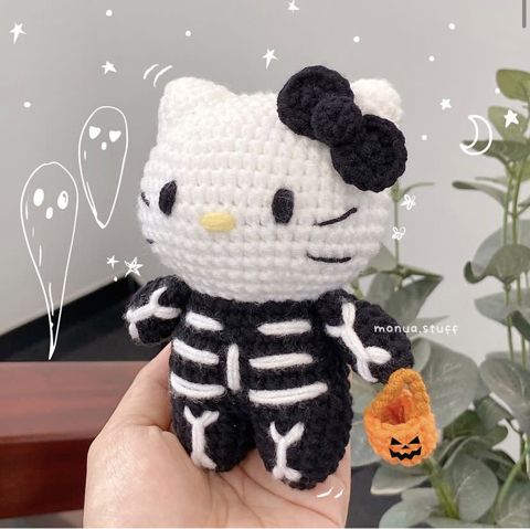 a hello kitty amigurt doll holding a pumpkin in her hand and wearing a skeleton costume