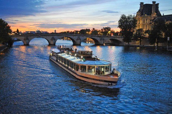 a boat is going down the river at dusk with people on it and bridges in the background