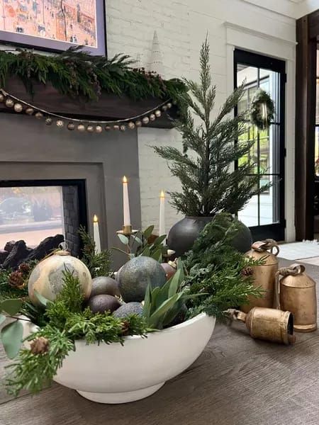 a white bowl filled with christmas decorations on top of a table next to a fireplace