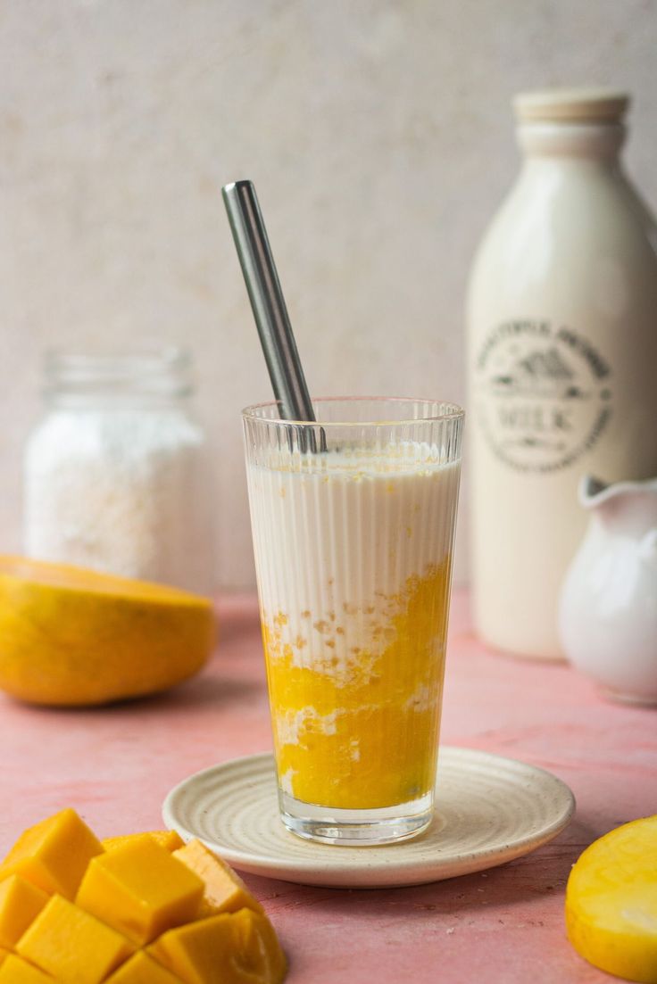 a glass filled with orange juice sitting on top of a table next to sliced mangoes