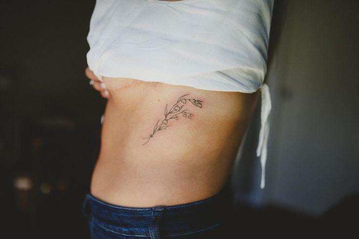 a woman's stomach with a flower tattoo on her left side ribcage