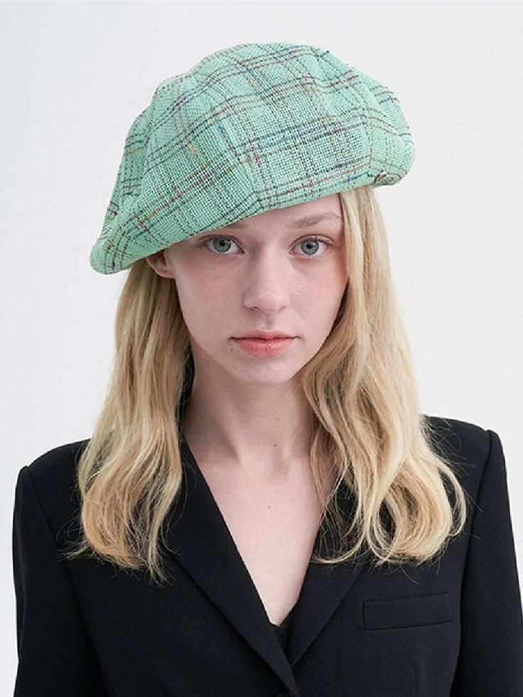 a woman with blonde hair wearing a green plaid newsboy hat and black blazer