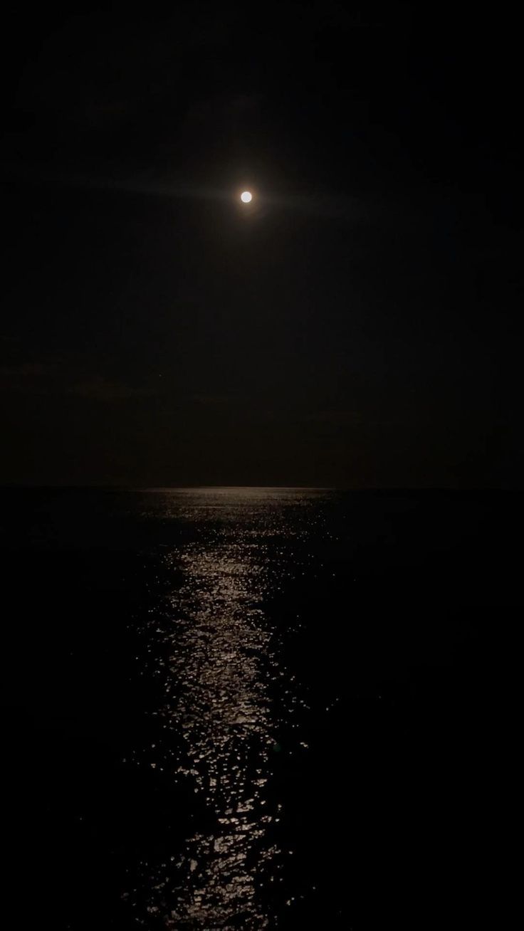 the moon shines brightly in the dark sky over the ocean at night, reflecting on the water