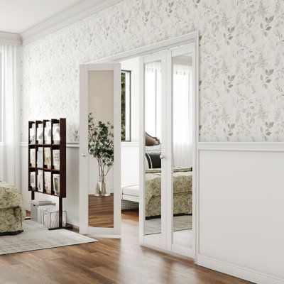 a bedroom with white walls and wood flooring next to a large mirror on the wall