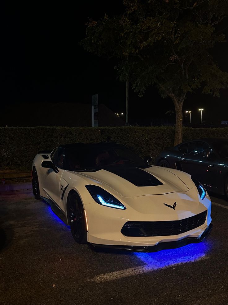 two white sports cars parked next to each other in a parking lot at night time