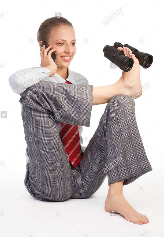 a woman in business attire sitting on the floor talking on her cell phone and holding binoculars - stock image