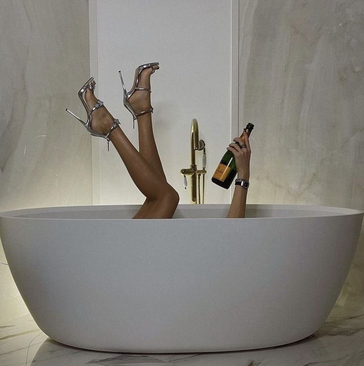 a woman laying in a bathtub with her feet up and holding two champagne bottles