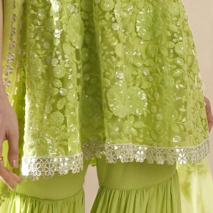 This exquisite Lime Green Embroidered Kurta Sharara Set exudes elegance and tradition. Crafted from soft net fabric, the strappy lime green kurta is adorned with intricate floral embroidery, shimmering silver sequins, and delicate thread work, with a hemline beautifully finished with cutwork gota lace for a refined touch. Teamed with a voluminous, flouncy sharara is gathered from the thigh, featuring a striking gota and mirror-embroidered hem that radiates glamour. A matching tulle dupatta grace Strappy Kurta, Georgette Kurta, Kurta Sharara Set, Kurta Sharara, Embroidered Hem, Sharara Set, Net Fabric, Net Dupatta, Thread Work