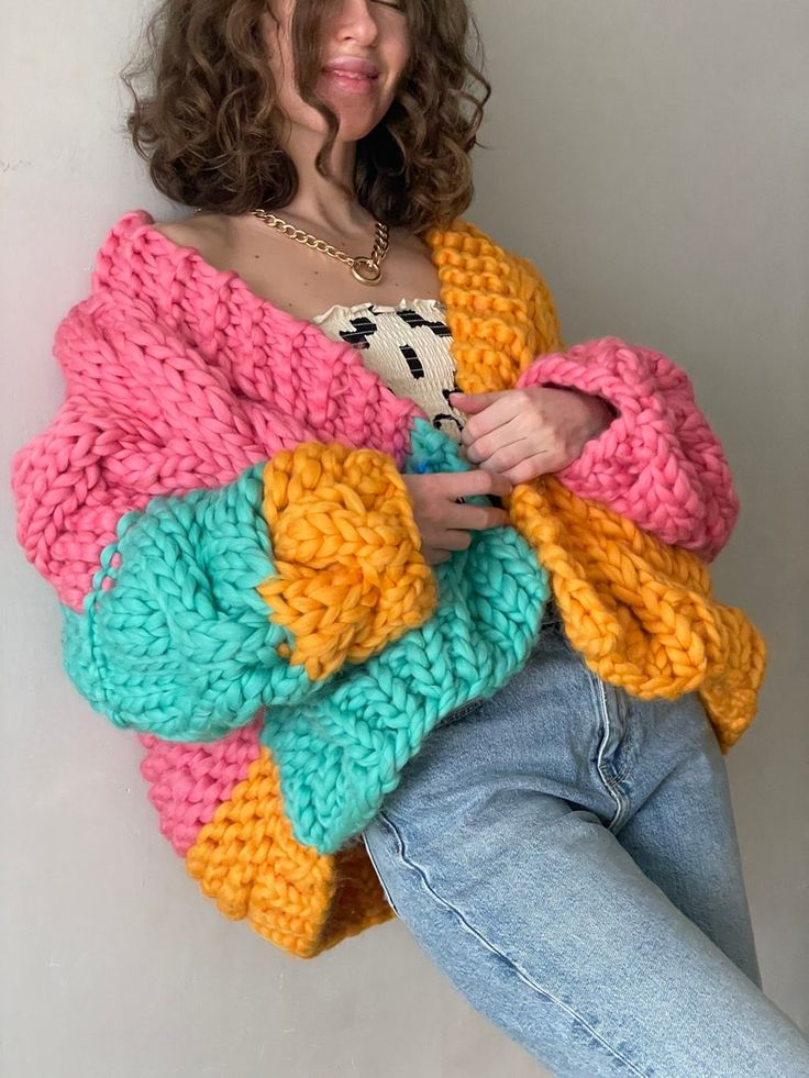 a woman sitting on the floor wearing a colorful knitted sweater and jeans with her hands in her pockets