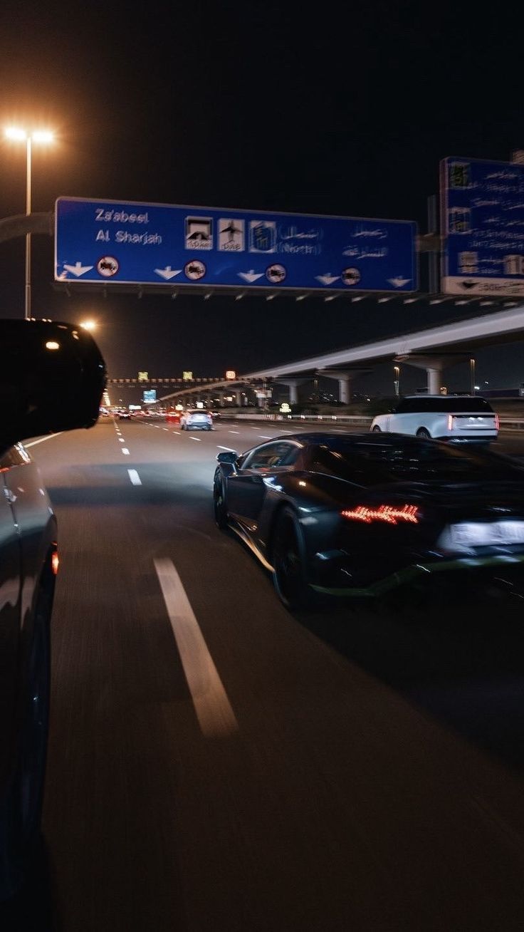 two cars driving down the highway at night with street signs in the backgroud