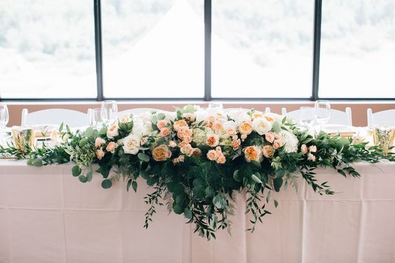 an arrangement of flowers and greenery is arranged on a table with white linens