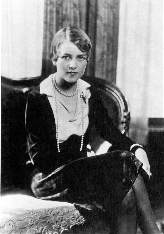 an old black and white photo of a woman sitting on a bed with her legs crossed