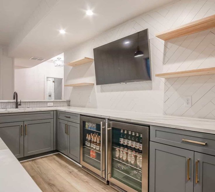 an empty kitchen with gray cabinets and white counter tops is pictured in this image, there is a television on the wall above the refrigerator