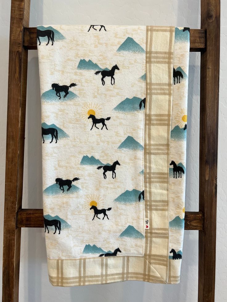 a blanket with horses on it hanging from a wooden ladder in front of a white wall