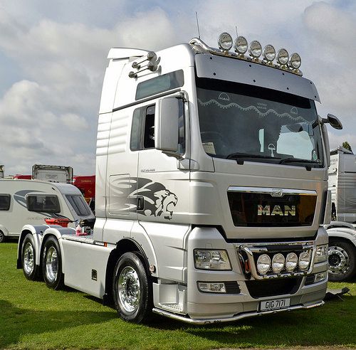 a silver semi truck parked on top of a lush green field next to other trucks