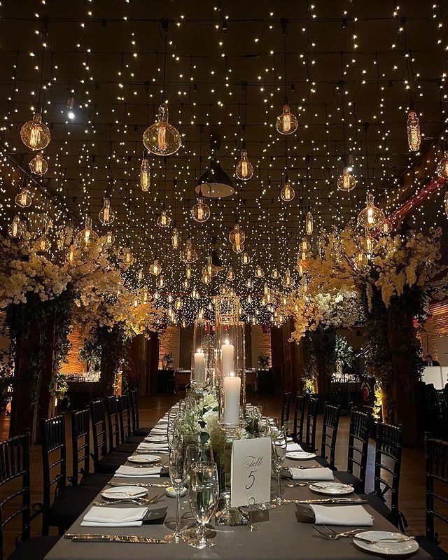 a long table is set with place settings and lite - up trees in the background