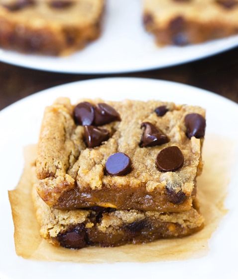 chocolate chip cookie bars stacked on top of each other in front of two plates with one slice cut out